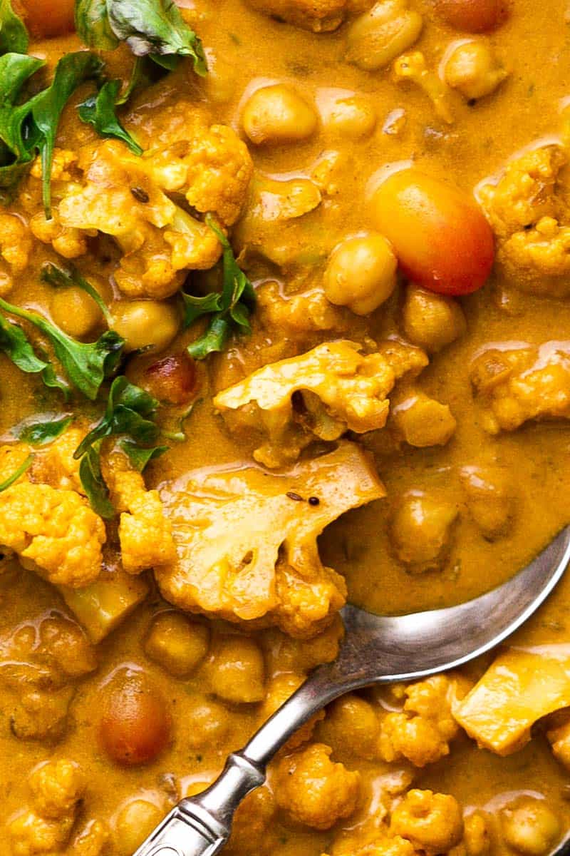 This is a classic coconut curry with tender cauliflower and soft chickpeas thats all made in one pot and has a simple mix of spices. That sauce is super addictive and you'll love how easy it is to make. It's vegan and gluten free, but you can easily add chicken, shrimp, lamb or beef if you prefer meat. #curry #sauce #coconut #cauliflower #dinner Closeup of Cauliflower Chickpea Coconut Curry with a spoon