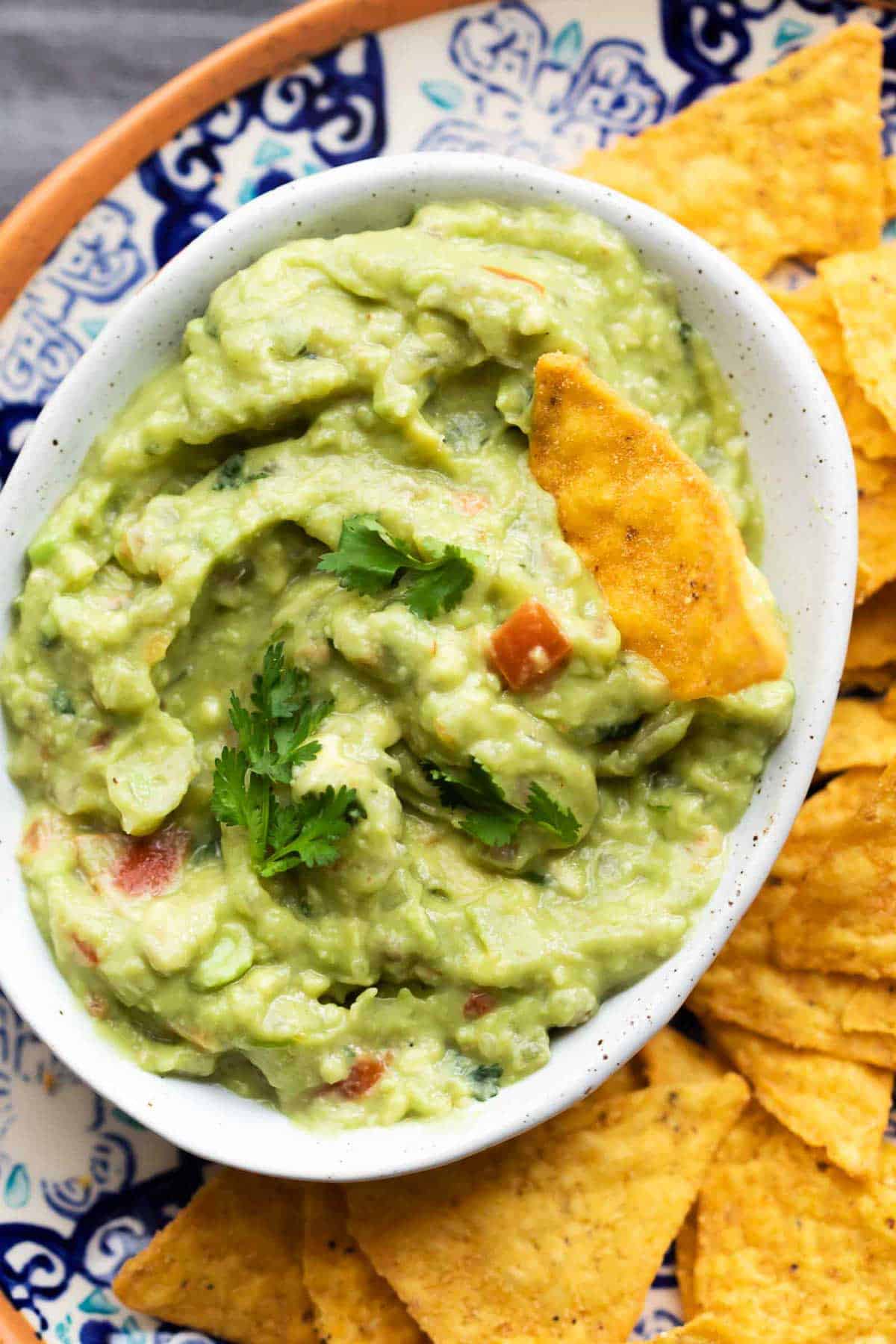 Crazy good homemade guacamole served in a white bowl with chips on the side.
