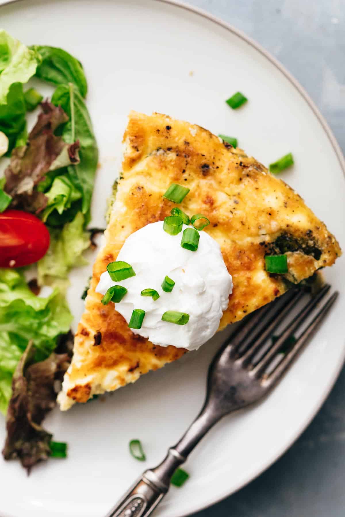A slice of spinach potato veggie frittata topped with a dollop of sour cream and chopped green onions