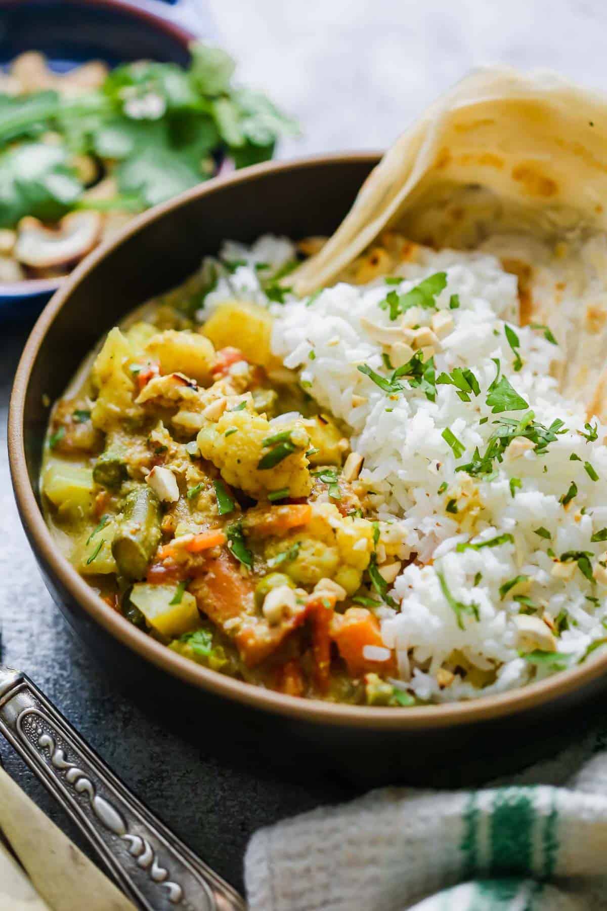 Vegetable Korma Curry served in a bowl with rice, malabar paratha and topped with crunchy cashews
