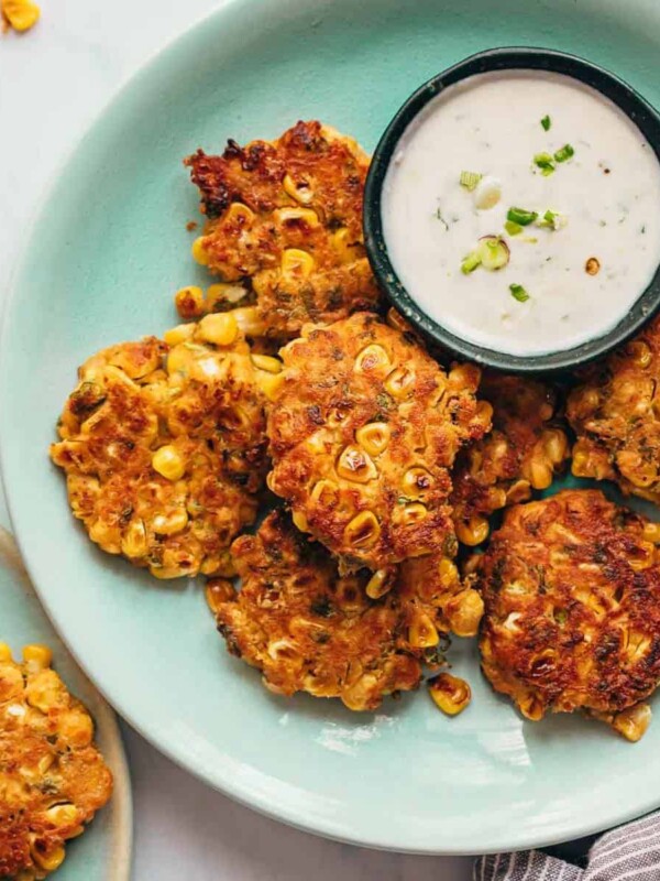 Mexican corn fritters served on a blue plate with a creamy dip on the side