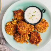 Mexican corn fritters served on a blue plate with a creamy dip on the side