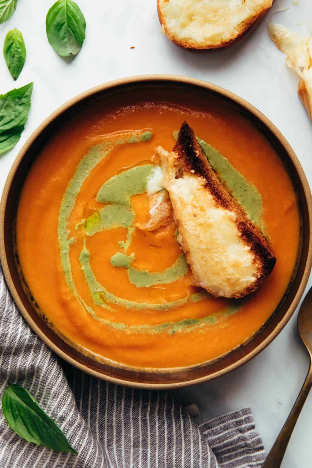 Roasted tomato pesto soup served in a bowl with toasted cheesy bread