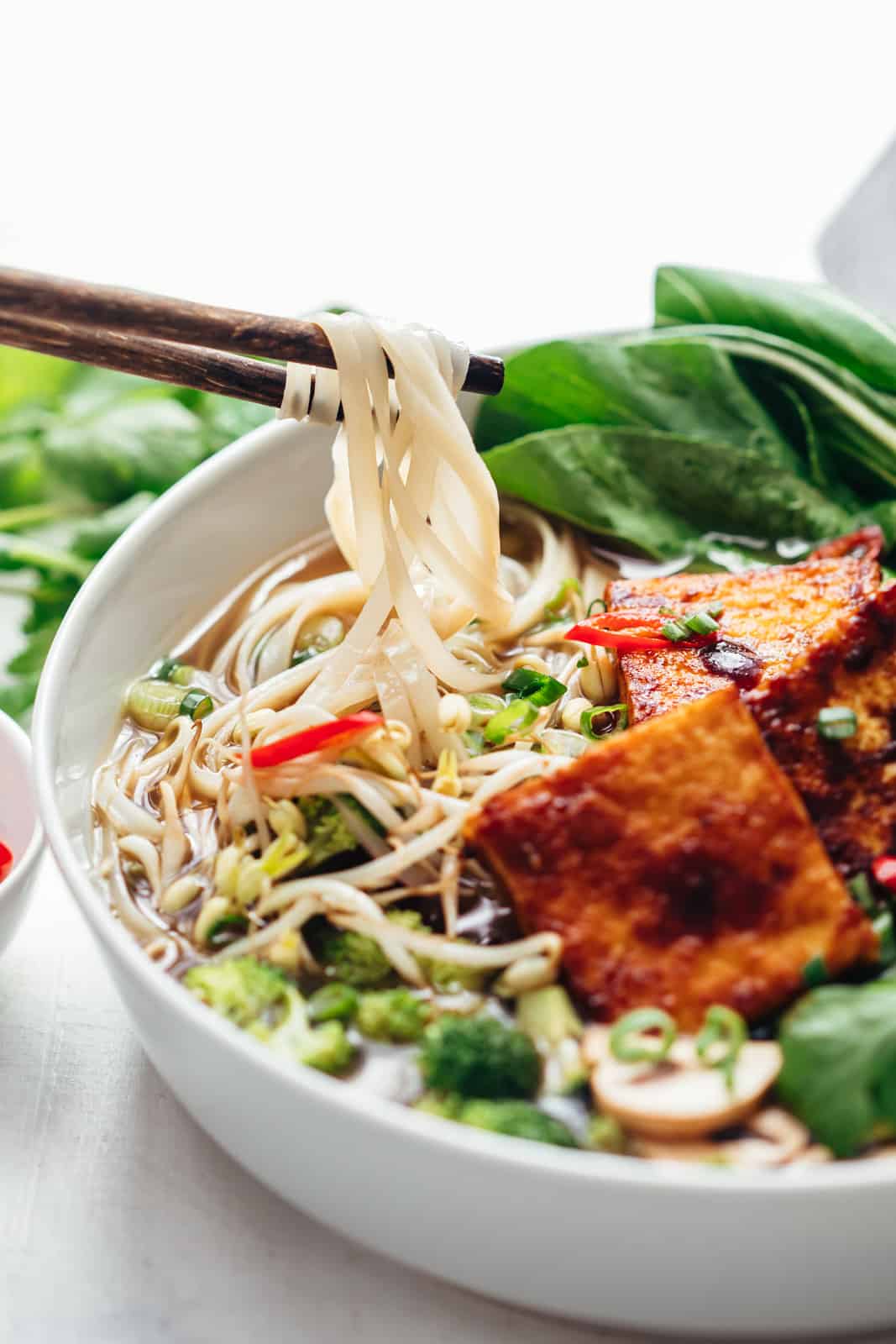 Using chopsticks to pick noodles from vegetarian pho soup bowl