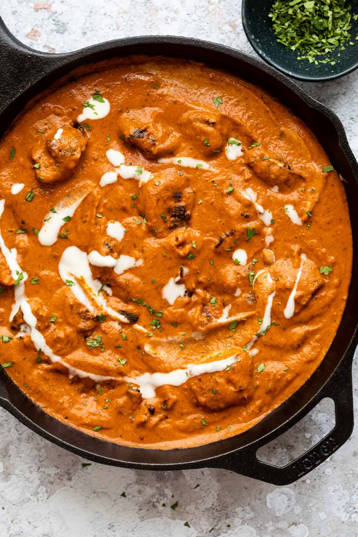 Butter chicken served in the pan it was cooked in with some chopped coriander on the side