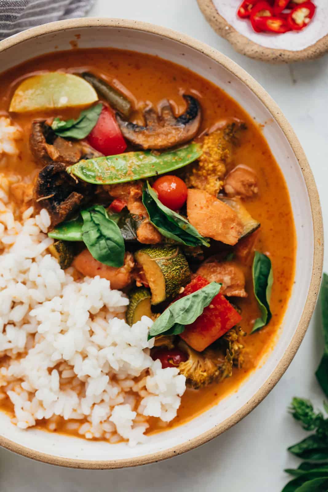 Closeup of Instant pot Thai chicken curry served in a bowl with rice, thai red chillies and lemon wedges
