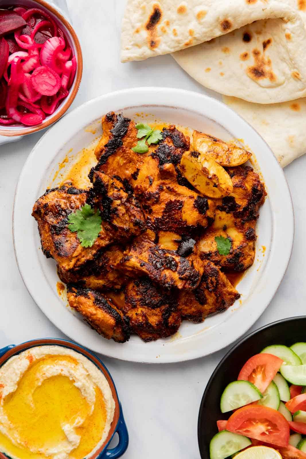 Chicken Shawarma laid out on a table along with pita, hummus, veggies, pickled beets and onions