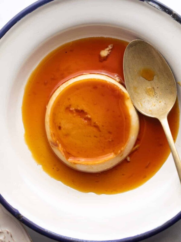 Closeup of coconut caramel custard served on a white plate with a blue edging and a spoon