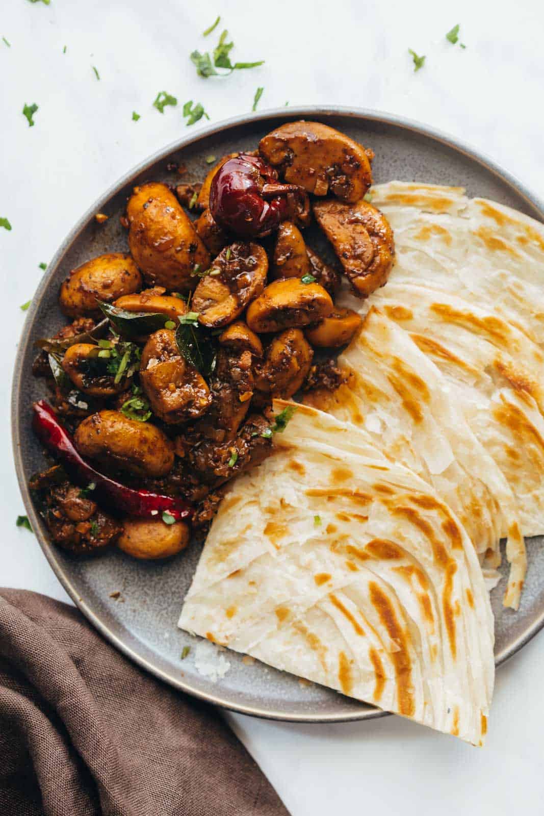 Mushroom pepper fry served on a grey plate with malabar parathas