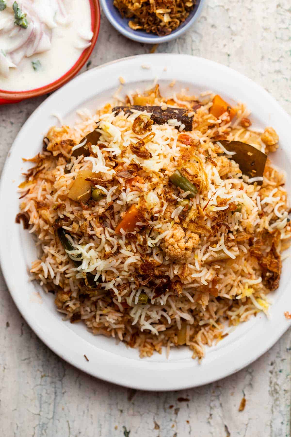 Veg Biryani served on a plate with raita and fried onions