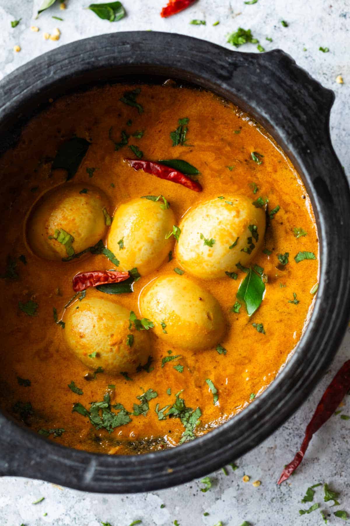 an image of south indian style egg curry in a black clay pot and garnished with coriander and curry leaves