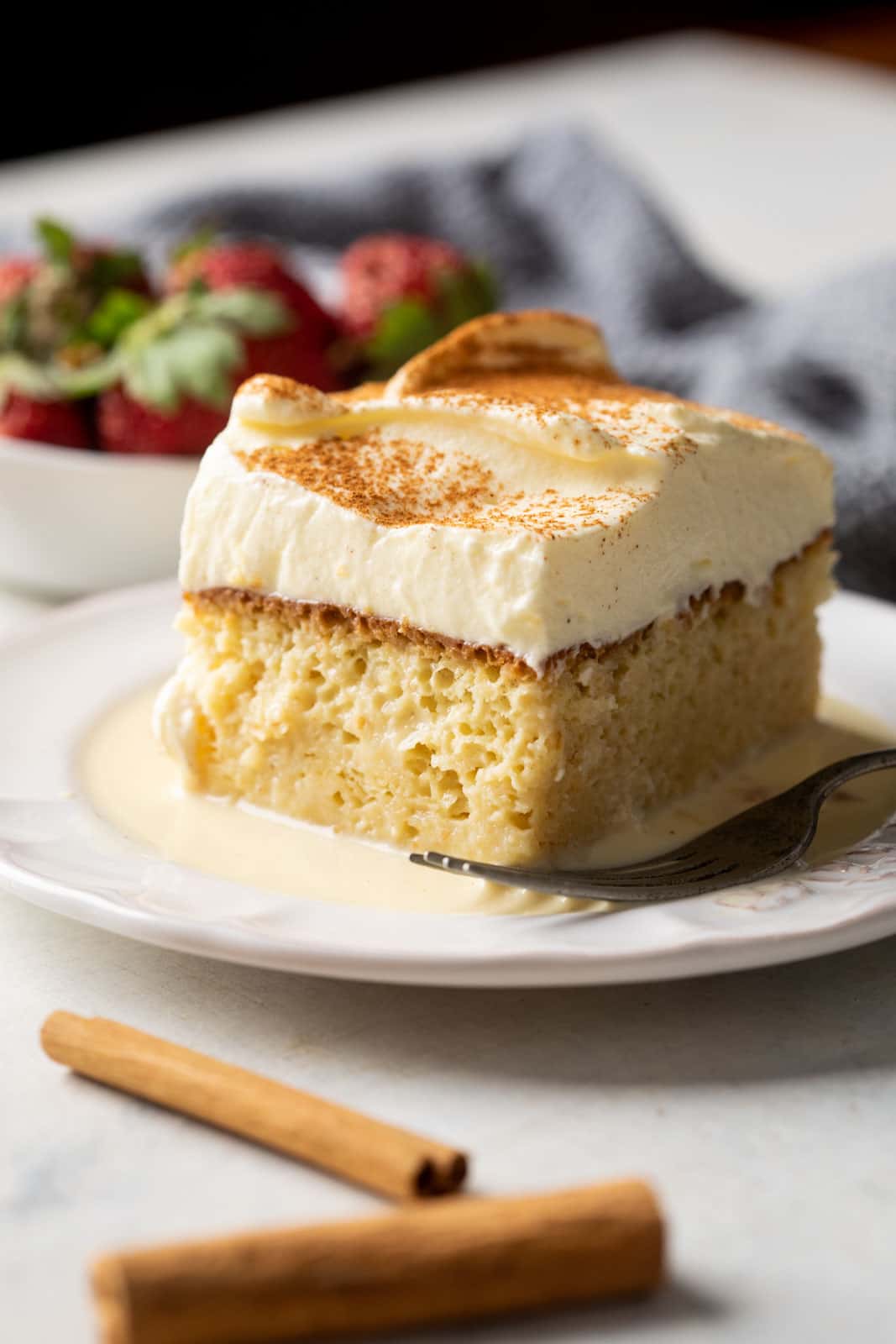 Eggnog tres leches served with strawberries on the side on a white plate