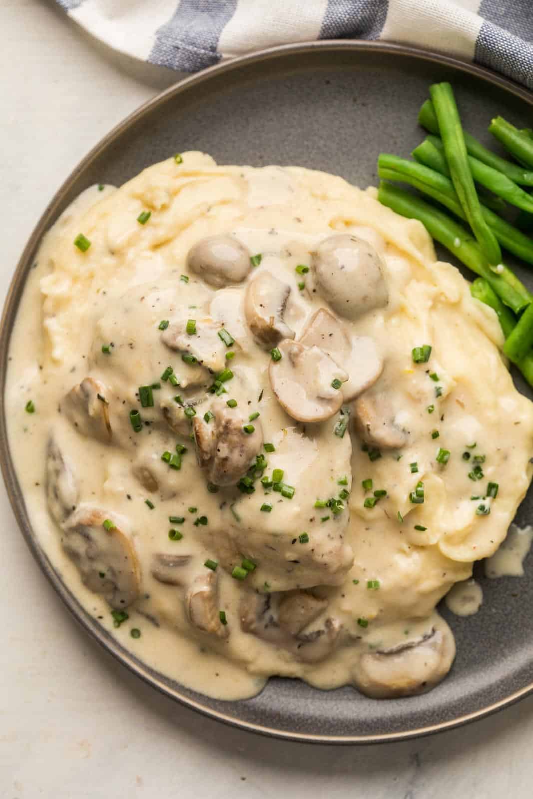 Instant Pot Chicken in mushroom sauce served over a bed of mashed potatoes on a grey plate with steamed green beans
