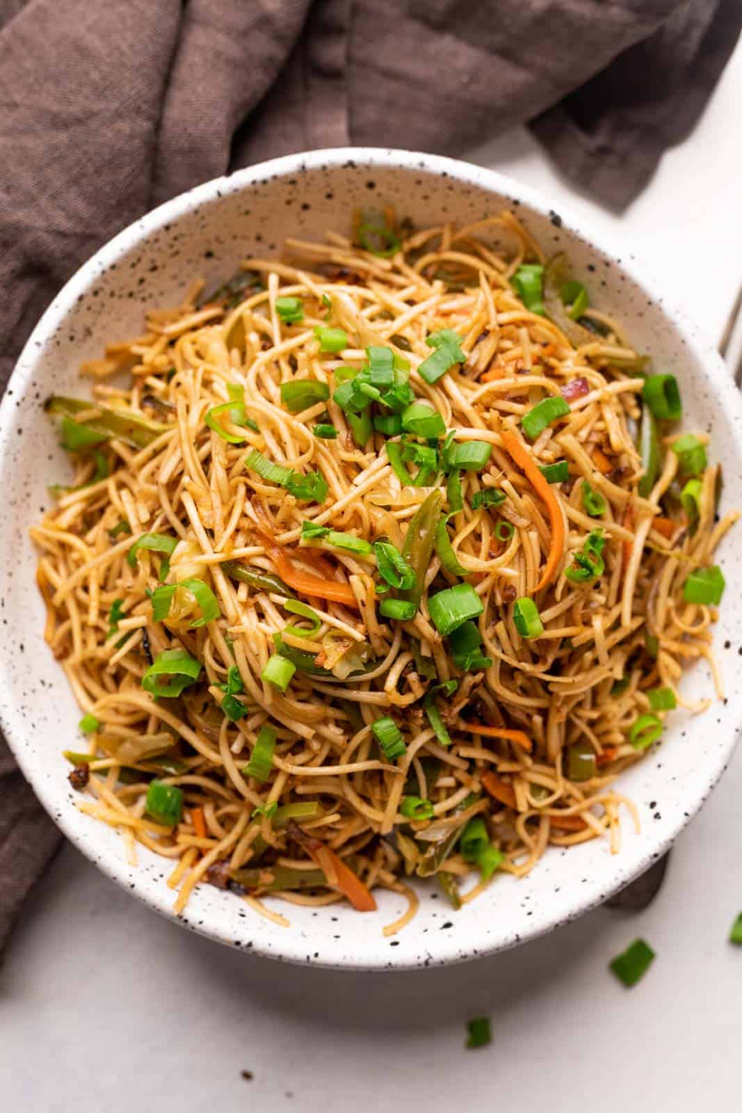 Vegetable hakka noodles served in a white speckled bowl