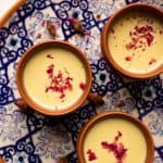 Thandai served in three mud glasses served on a colourful blue plate with rose petals on top