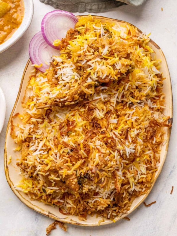 Mutton biryani served on a platter with sliced onions, raita and mirchi salan