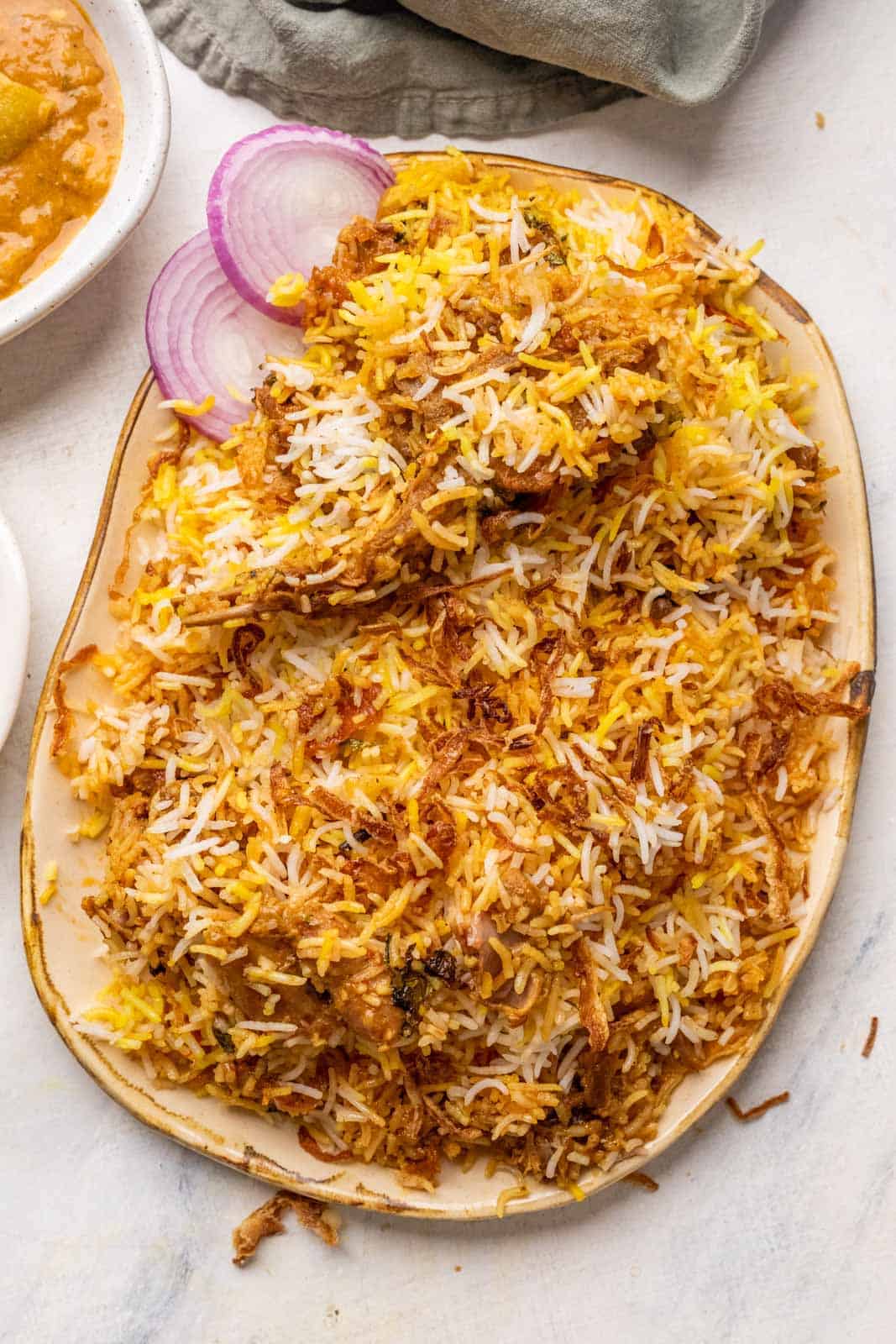 Mutton biryani served on a platter with sliced onions, raita and mirchi salan