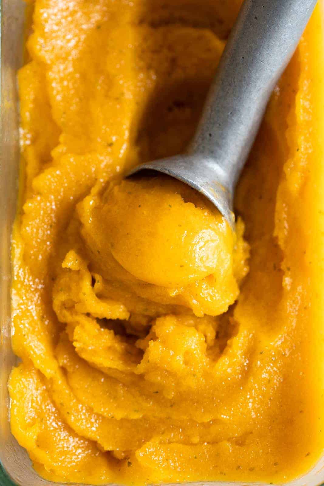 Mango sorbet being scooped out with an ice cream scooper from the container
