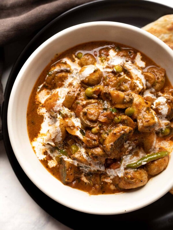 Mushroom masala served in a white bowl with a drizzle of cream on top with paratha on the side