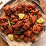 Chicken 65 served on a plate with lime wedges, fried curry leaves and green chillies