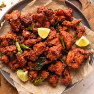 Chicken 65 served on a plate with lime wedges, fried curry leaves and green chillies