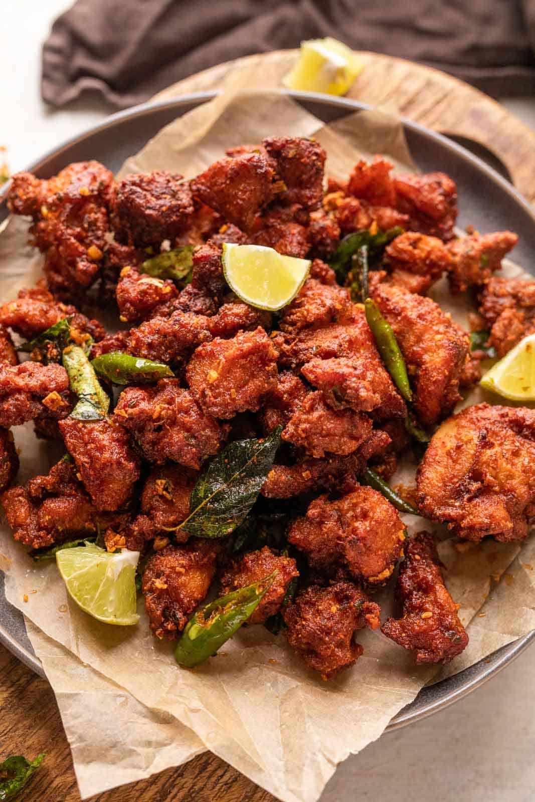 Chicken 65 served on a plate with lime wedges, fried curry leaves and green chillies