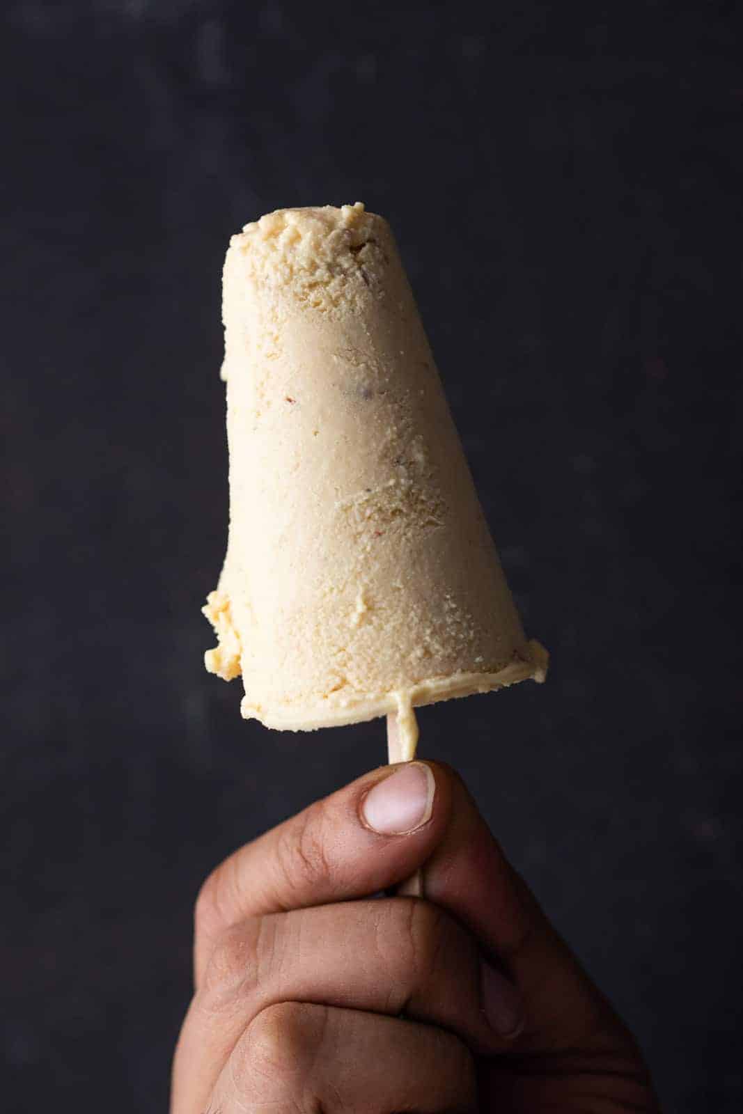 A hand holding malai kulfi against a black background