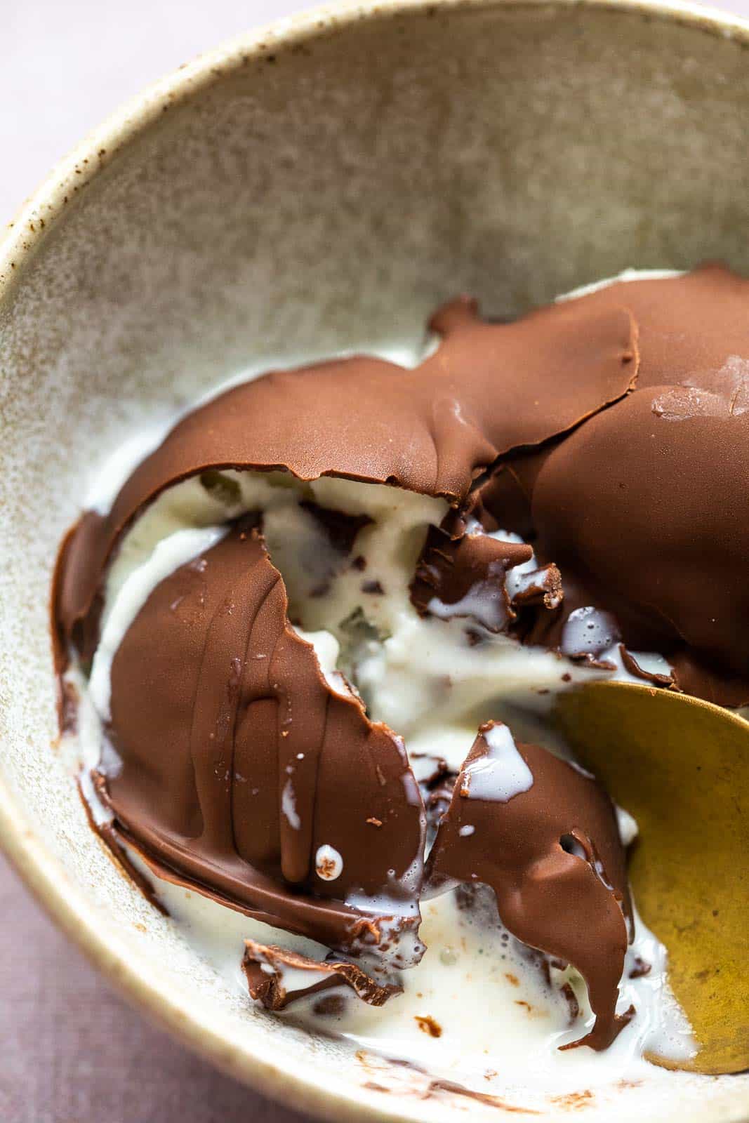 Cracked chocolate magic shell with vanilla ice cream to show the texture in a brown bowl