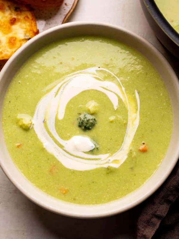Healthy broccoli soup served in a white bowl with garlic bread on the side