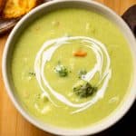 Healthy broccoli soup served in a white bowl with garlic bread on the side