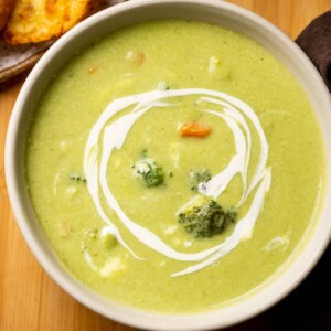 Healthy broccoli soup served in a white bowl with garlic bread on the side