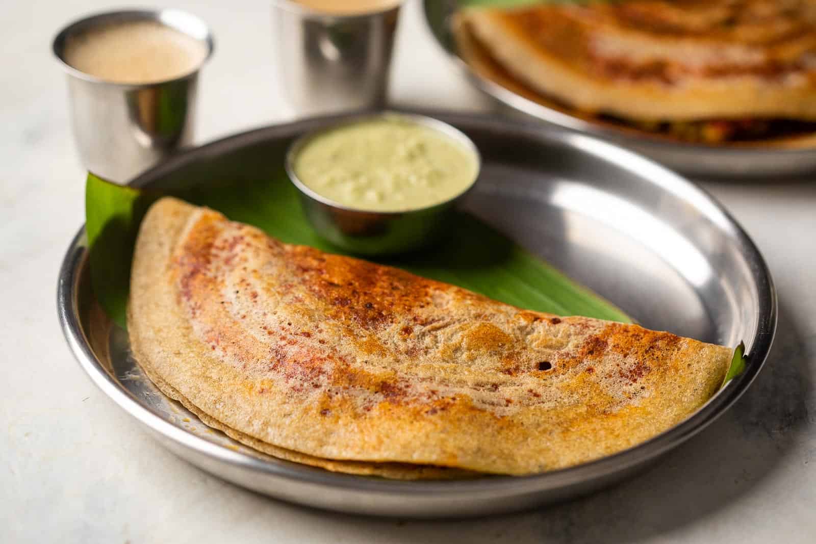 Millet mysore masala dosa served on a steel plate with chutney and filter coffee