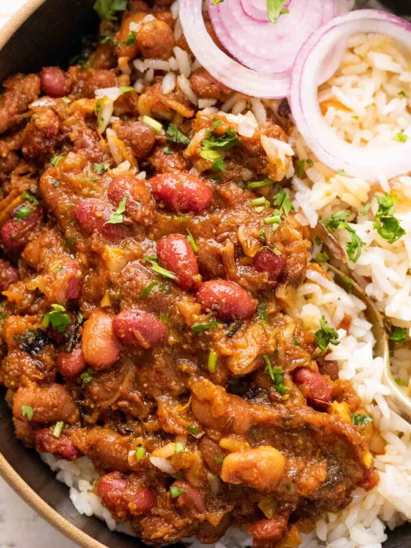 Rajma Masala served in a bowl on top of rice with sliced onions on the side