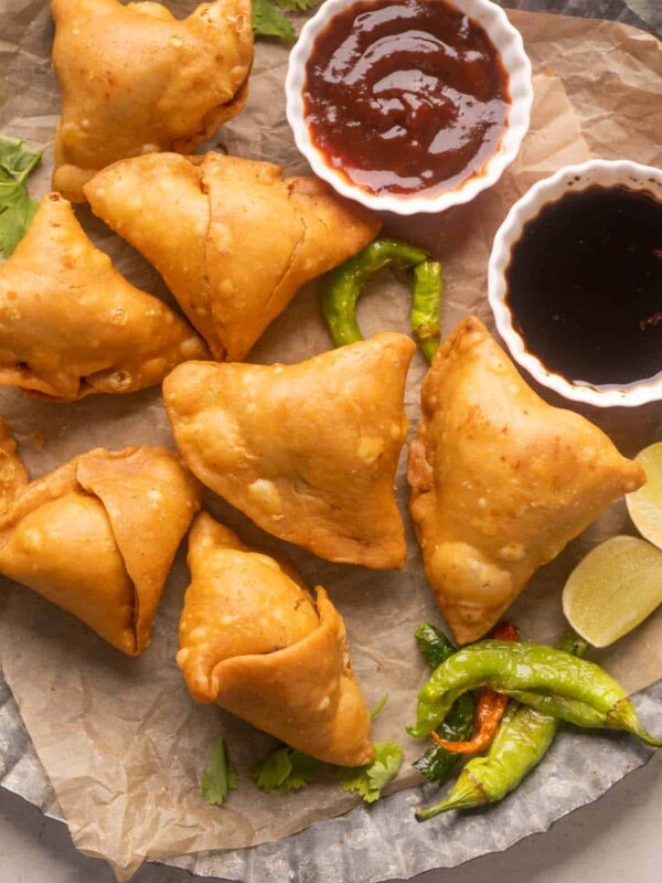 Samosas placed on a plate with ketchup, chutney, fried chillies, chai and lime