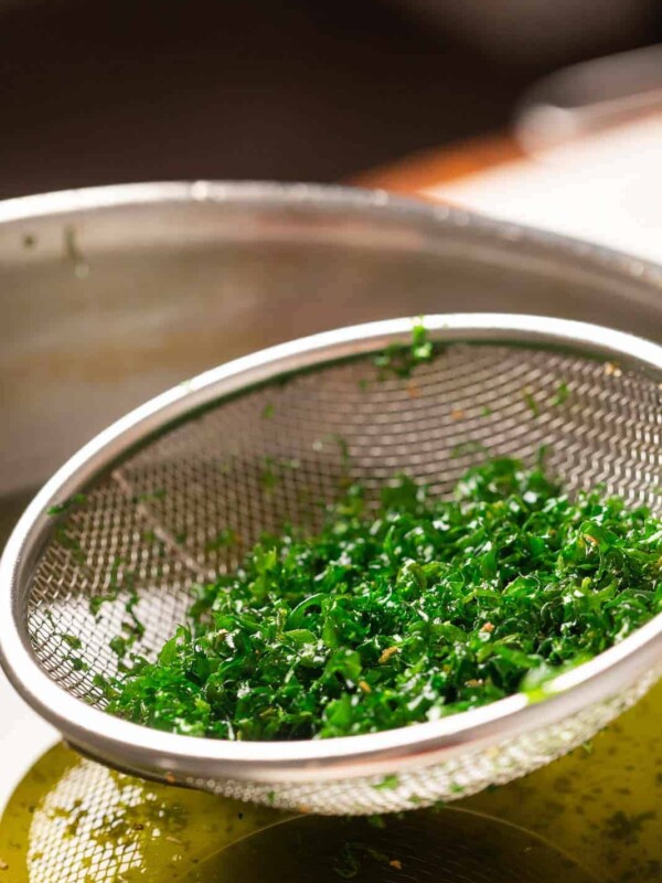 Crispy fried spinach being taken out of hot oil in a strainer