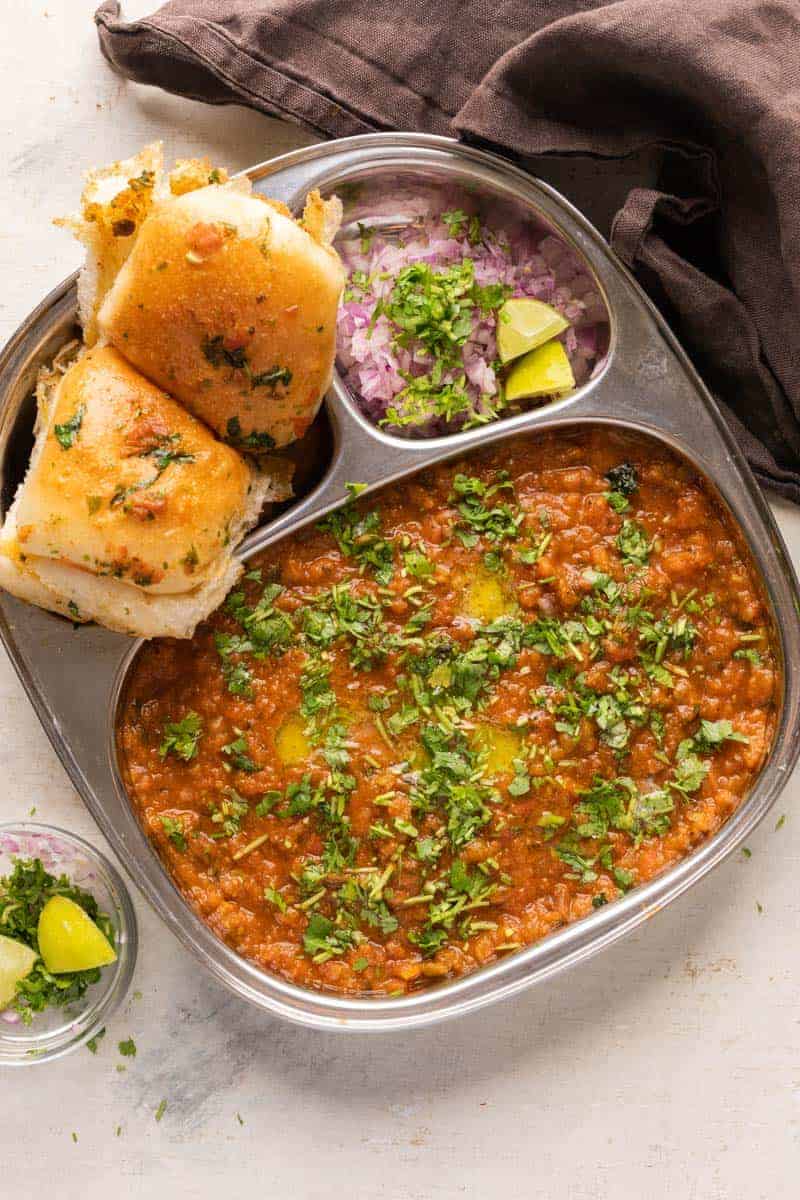 Pav Bhaji served in a steel plate with ladi pav, onions and coriander on the side