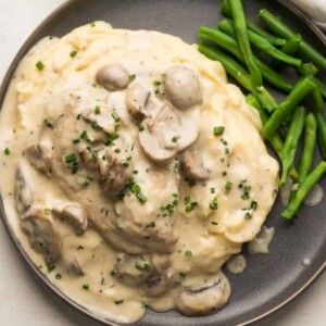 Chicken in served over mashed potatoes with mushroom sauce spooned over and steamed green beans on the side