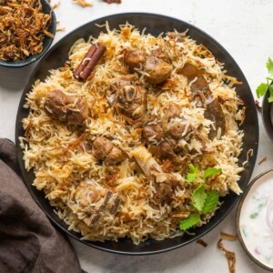 Mutton Yakhni Pulao served on a plate with fried onions and raita on the side