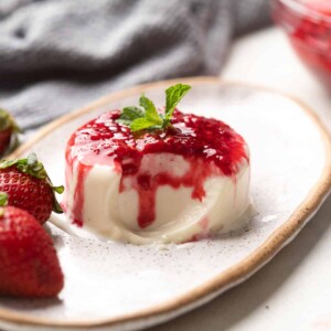Panna Cotta served on a white platter with raspberry coulis on top and a twig of mint