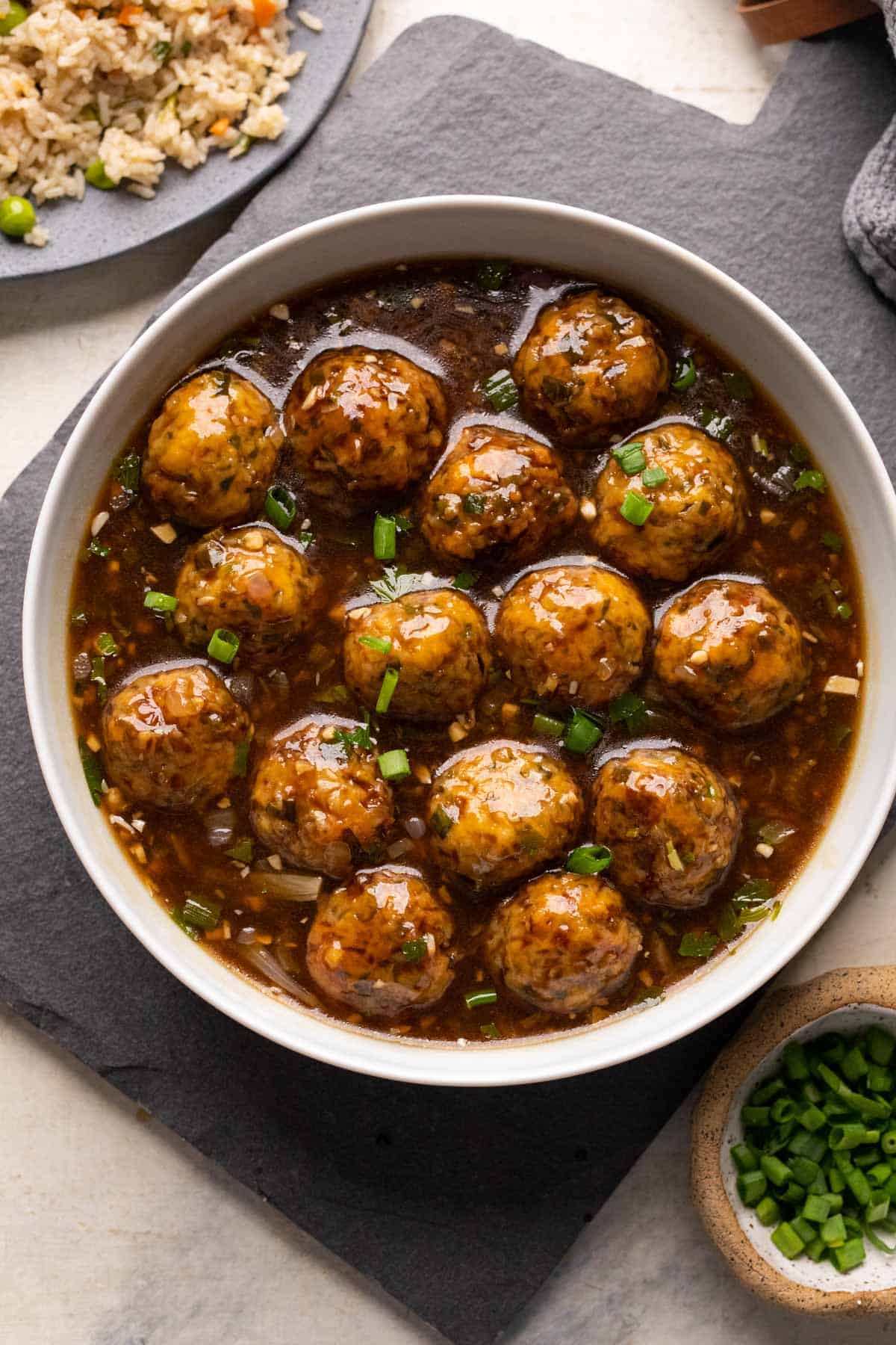 Veg manchurian served in a white bowl with fried rice and spring onions on the side