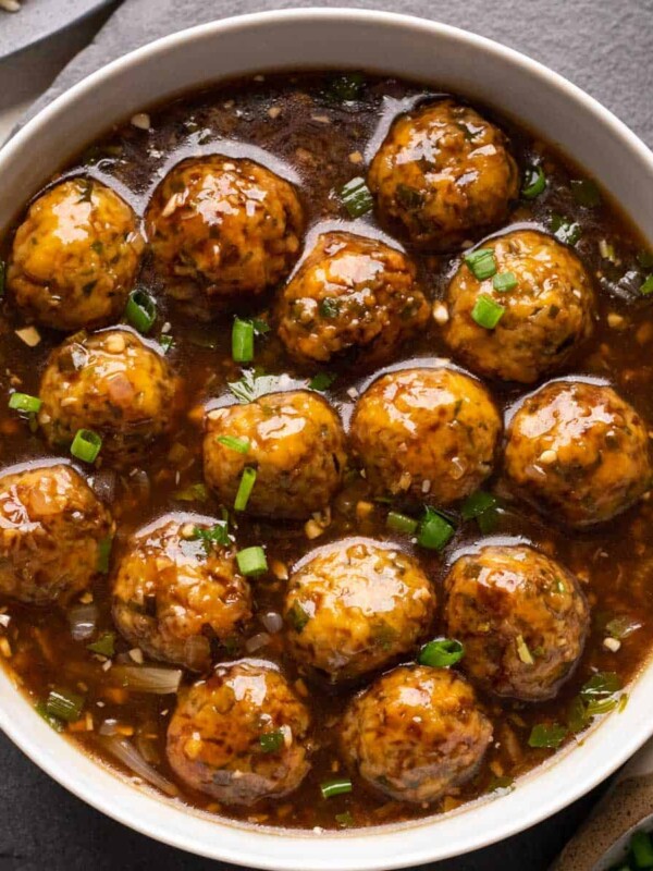 Veg manchurian served in a white bowl with fried rice and spring onions on the side