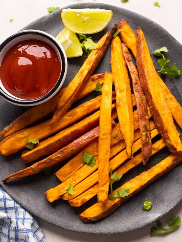 Picture of baked sweet potato fries served on a grey plate with ketchup and lime wedges on the side