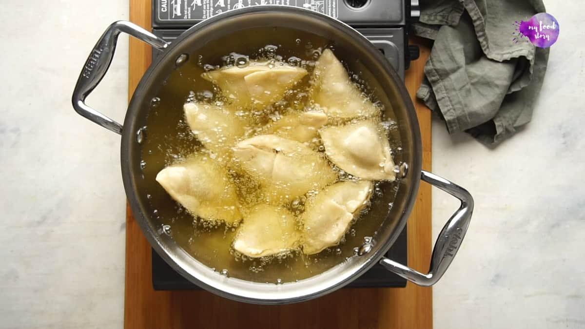 Samosas being fried in a pan of hot oil