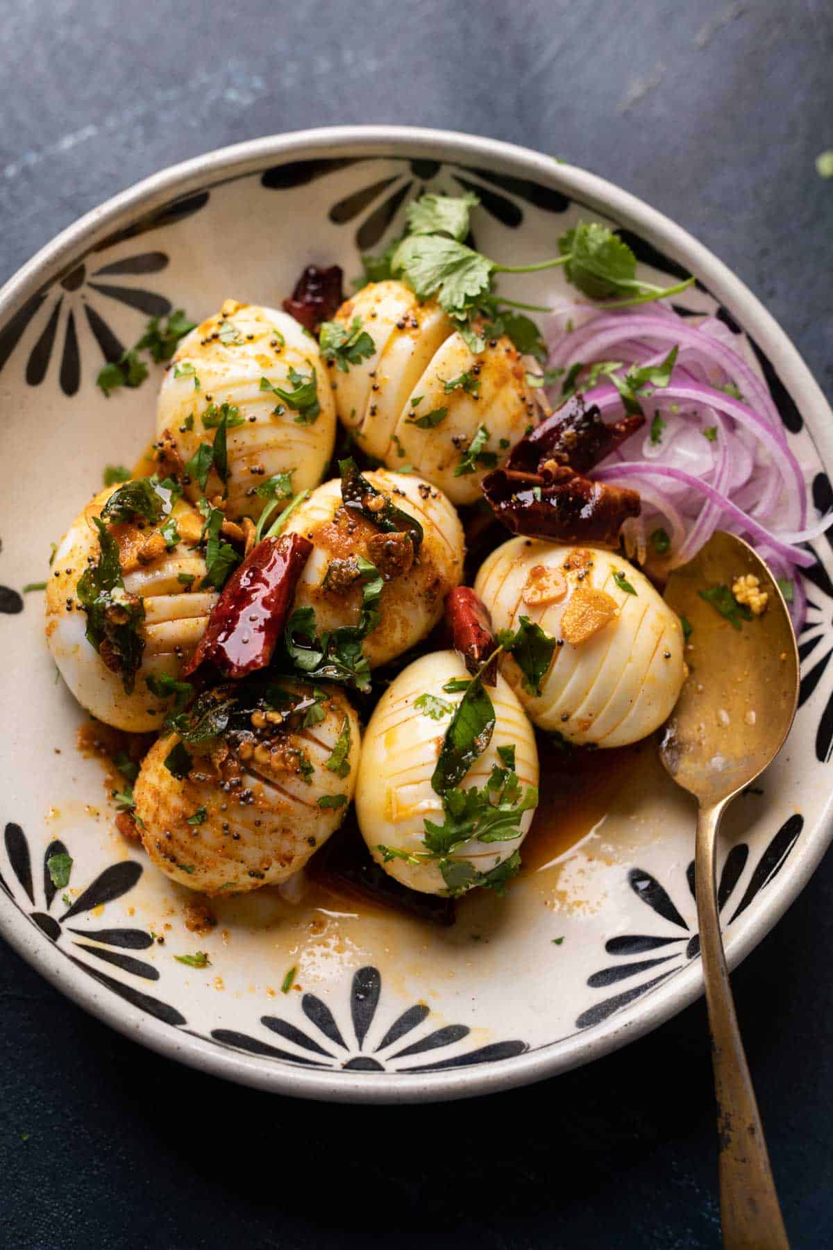 Egg tadka served in a black and white bowl with sliced onions on the side