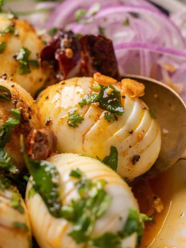 Close up of hasselback egg tadka with a spoon and sliced onions on the side