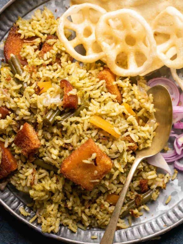 Rice bath served in a grey plate with fryums, poppdum and onions on the side