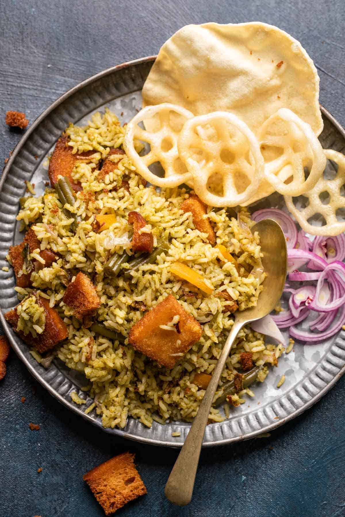 Rice bath served in a grey plate with fryums, poppdum and onions on the side