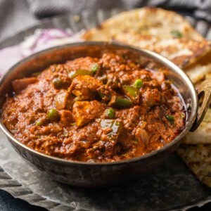 Picture of veg kolhapuri served in a copper kadhai on a plate with onions and naan