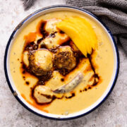 Mango Kadhi served in a blue and white enamel bowl with mango slices and tadka on top