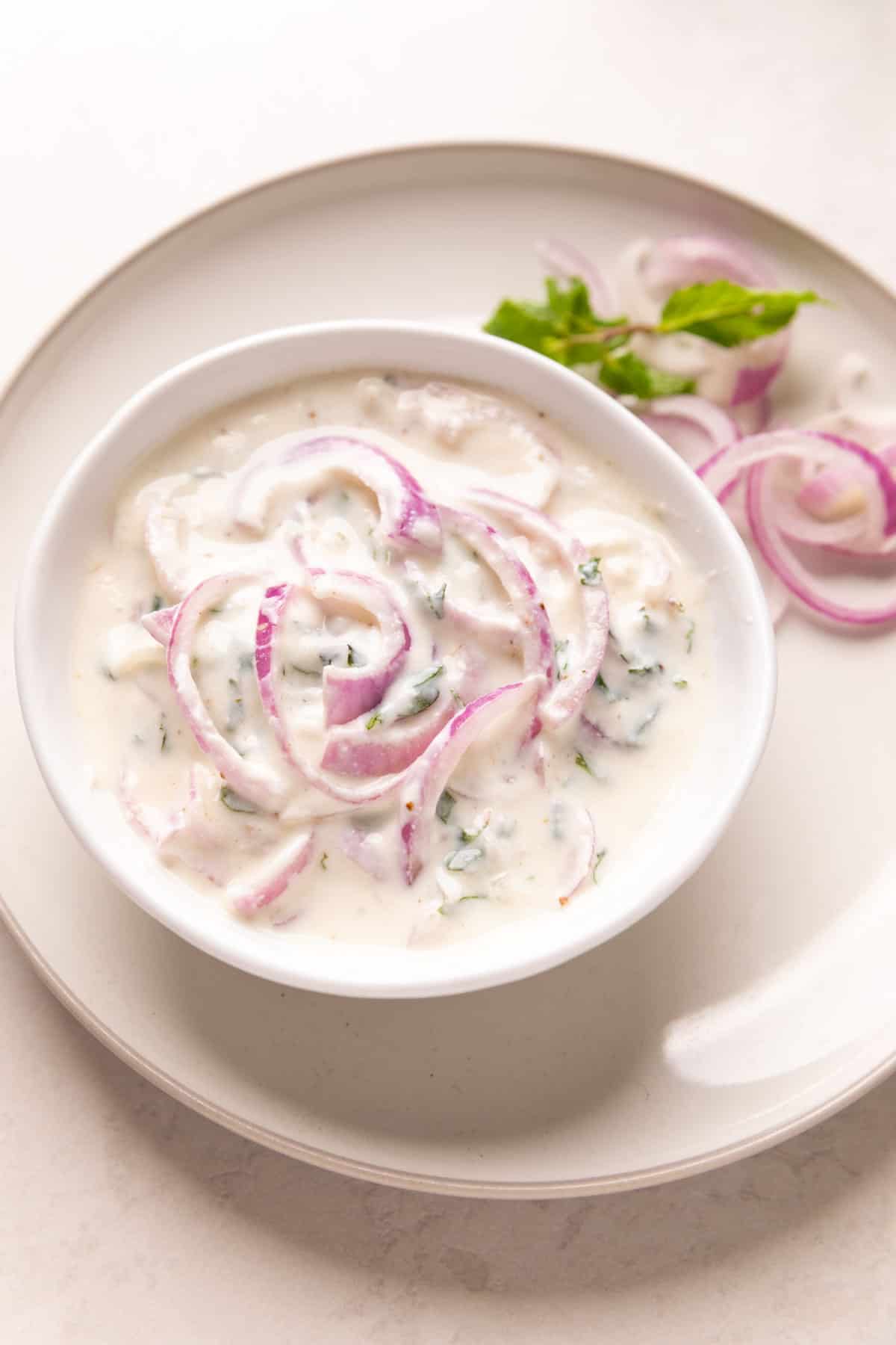 Picture of onion raita served in a white bowl on a white plate